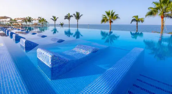 Infinity-Pool mit integrierten Liegen im Riu Gran Canaria, Palmen und Meer im Hintergrund.