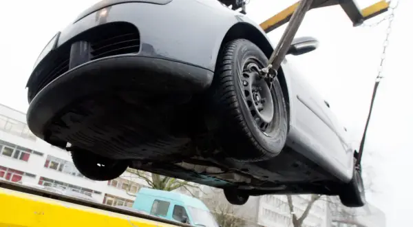 Ein graues Auto wird mit Gurten und Ketten von einem Abschleppwagen gehoben. Es muss wohl abgeschleppt werden.