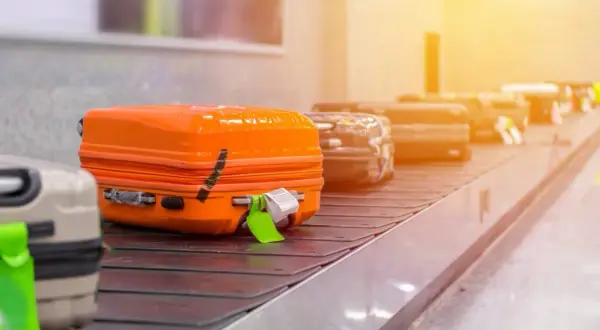 Koffer auf Gepäckband. Ein orangefarbener Koffer mit Klebeband und Anhänger. Hier beginnt die Geschichte, warum Koffer verloren gehen.