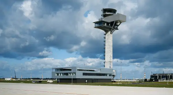 Moderner flughafen tower mit Glasfronten und einem Betonpfeiler, der über das Rollfeld ragt.