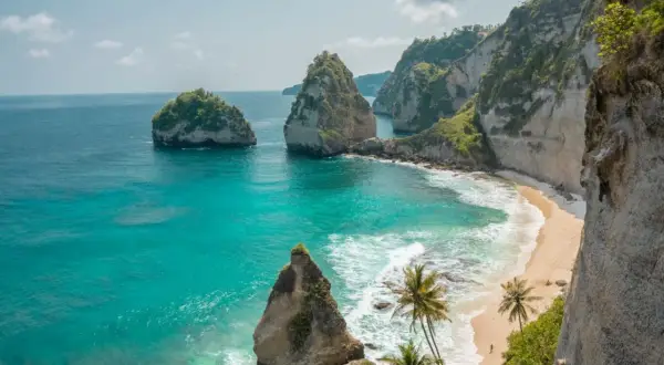 Traumhafter Urlaub auf Bali: Türkisblaues Meer trifft auf einsame Sandstrände und steile Felsklippen mit Palmen. Ein Paradies!