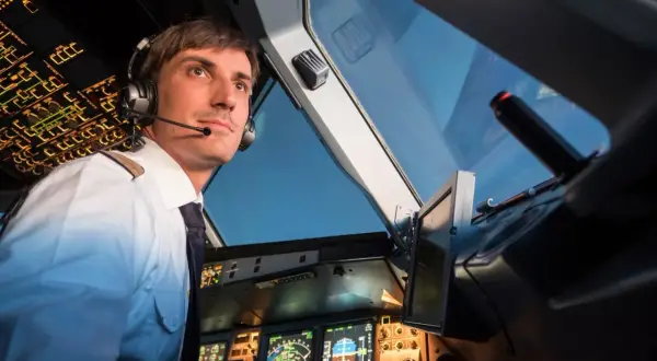 Ein Pilot im Cockpit, der aufmerksam auf die Instrumente blickt. Er trägt Kopfhörer und eine Uniform, wie ein deadhead pilot, der auf seinen Einsatz wartet.