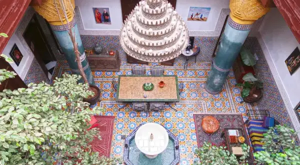 Ein Innenhof in Marrakesch mit Mosaikböden, einer Fontäne, üppiger Vegetation und einem Kronleuchter. Perfekt für einen entspannten Urlaub.