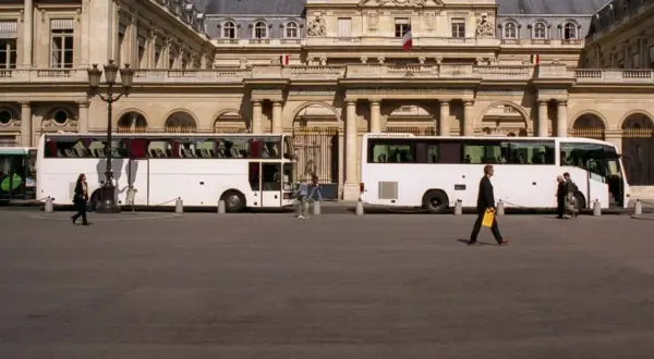 Weiße Reisebusse vor einem prächtigen Gebäude. Eine Frau geht vorbei. Wie kommt man am besten nach Paris? Mit dem Bus!