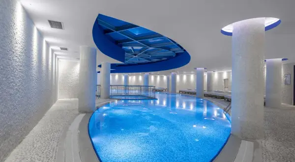 Ein luxuriöses Schwimmbad mit blau beleuchtetem Wasser, umgeben von weißen Säulen und Mosaikwänden. Ein Ort, der wie ein **rubi platinum sign** für Entspannung wirkt.