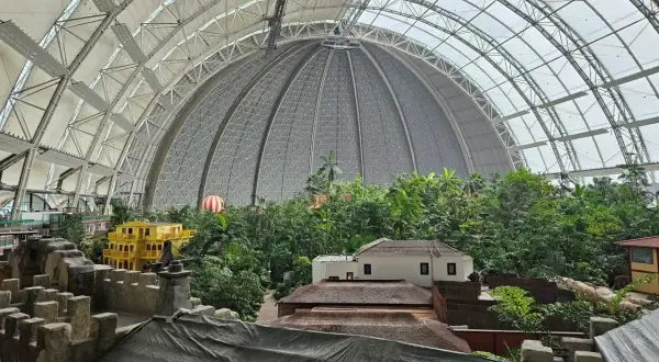 Tropische Insel-Atmosphäre unter riesiger Kuppel. Gelbes Gebäude, Häuser, üppige Vegetation. Perfekt für eine Packliste Tropical Island.