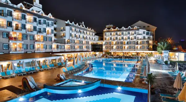 Nachtansicht des Diamond Beach Hotel & Spa mit beleuchteten Pools, Rutschen und Liegestühlen.