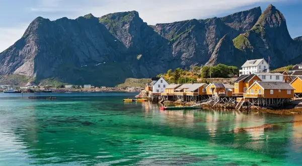 Idyllische Fischerhäuser auf Stelzen am kristallklaren Wasser vor majestätischen Bergen. Ein perfekter Urlaub in Norwegen.