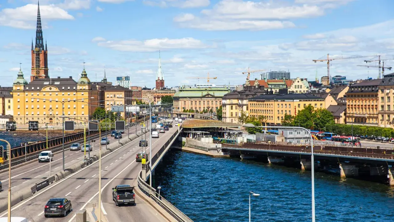 Blick auf die Skyline von Stockholm mit einem Fluss und einer Autobahn, auf der Autos fahren. Das Parken in Stockholm ist hier gut zu sehen.