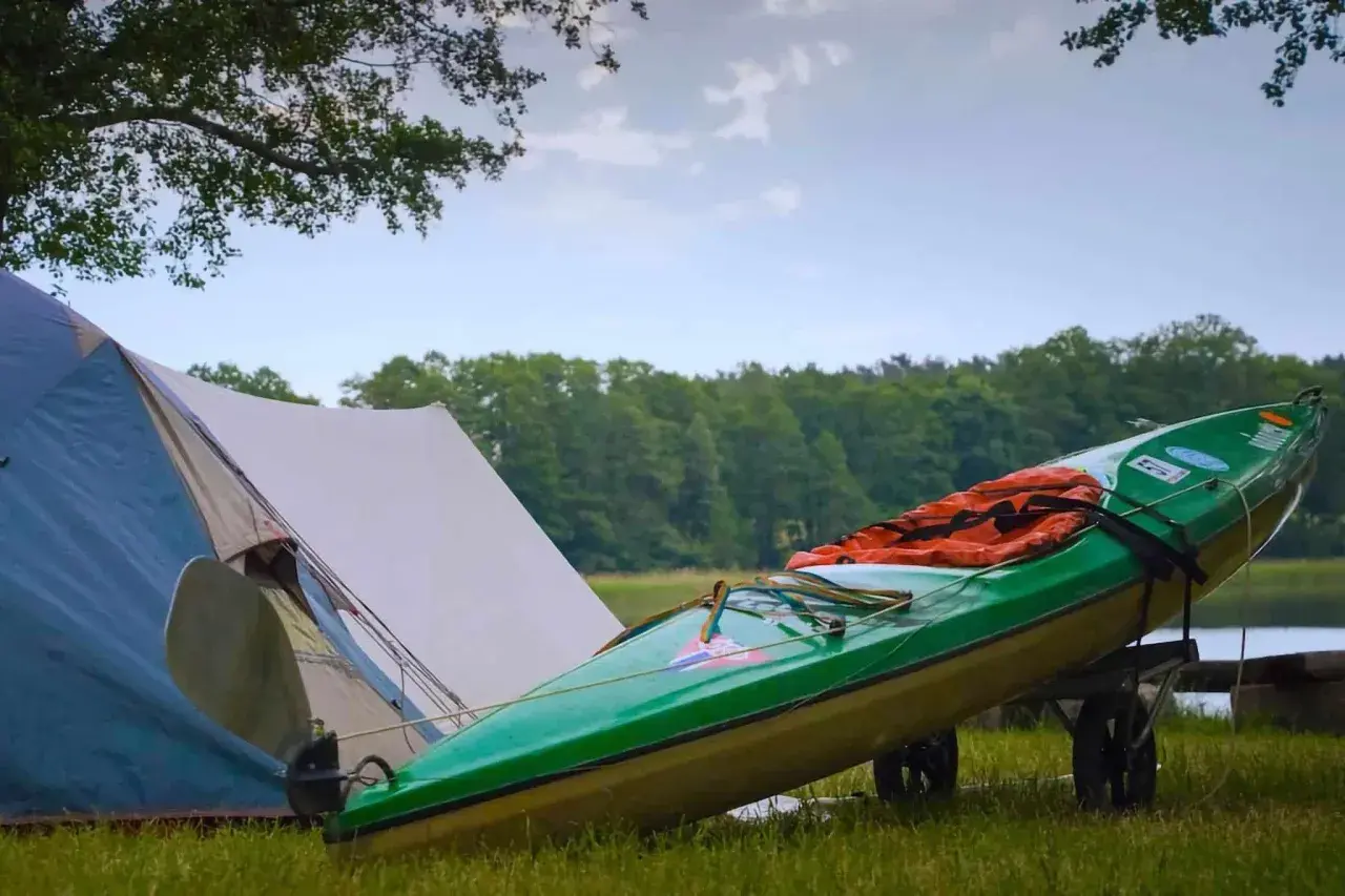 Grünes Kajak mit Schwimmweste auf einem Anhänger neben einem Zelt. Perfekte zelt gadgets für ein Abenteuer am See.