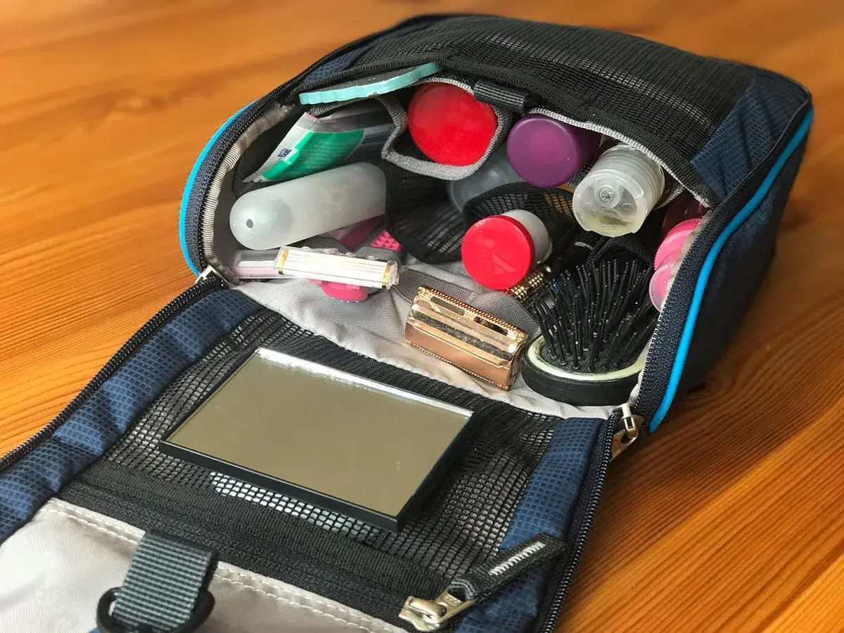 Offener Kulturbeutel mit Kosmetikartikeln: Zahnbürste, Rasierer, Kamm, Spiegel und diverse Fläschchen. Perfekte Packliste für unterwegs.