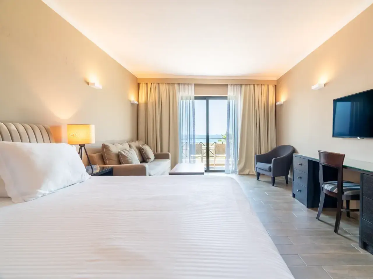 Gemütliches Zimmer im sentido pelagos suites & spa mit Meerblick vom Balkon. Einladendes Bett, Sofa und Schreibtisch.