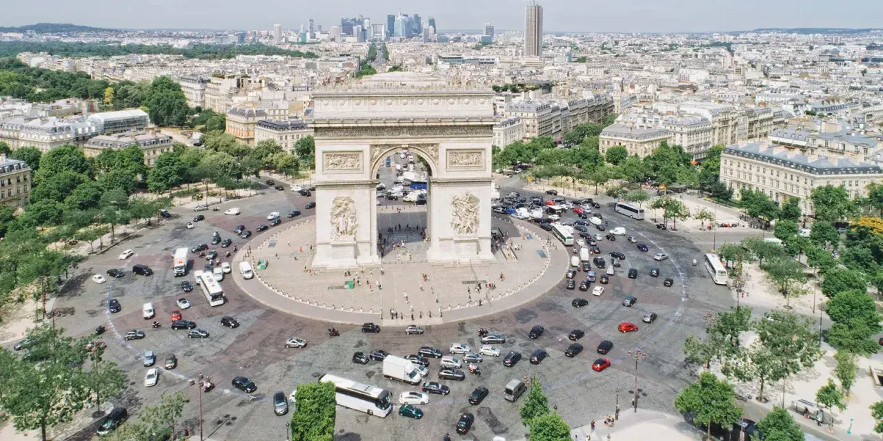 Ein Auto fährt durch Paris, vorbei am Triumphbogen. Die Skyline von Frankfurt ist in der Ferne zu sehen.