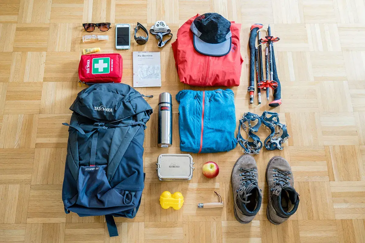 Packliste Bergtour: Rucksack, Wanderschuhe, Steigeisen, Jacken, Mütze, Wanderstöcke, Erste-Hilfe-Set, Thermoskanne, Handy, Sonnenbrille, Karte.