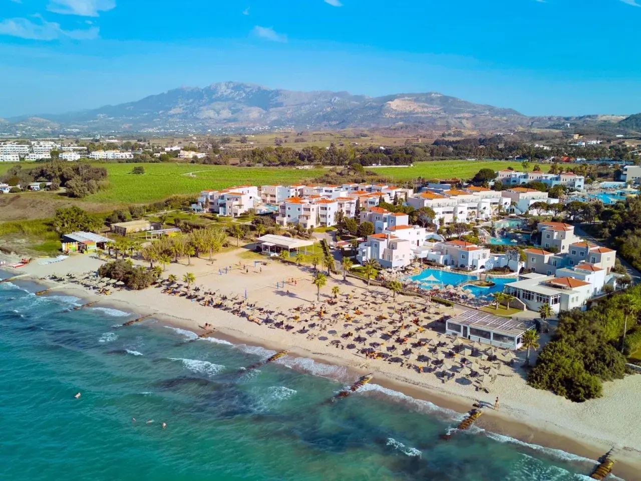 TUI Magic Life Marmari Palace: Traumhafter Strandurlaub mit türkisblauem Meer, weißen Gebäuden und Bergen im Hintergrund.