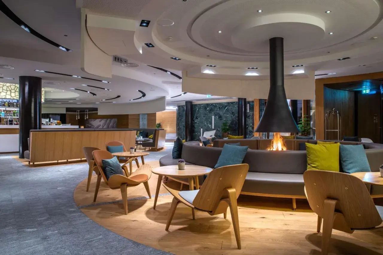 Gemütliche Lounge mit Kaminfeuer im Radisson Blu Hotel Andermatt. Moderne Sitzmöbel und Holzakzente laden zum Verweilen ein.