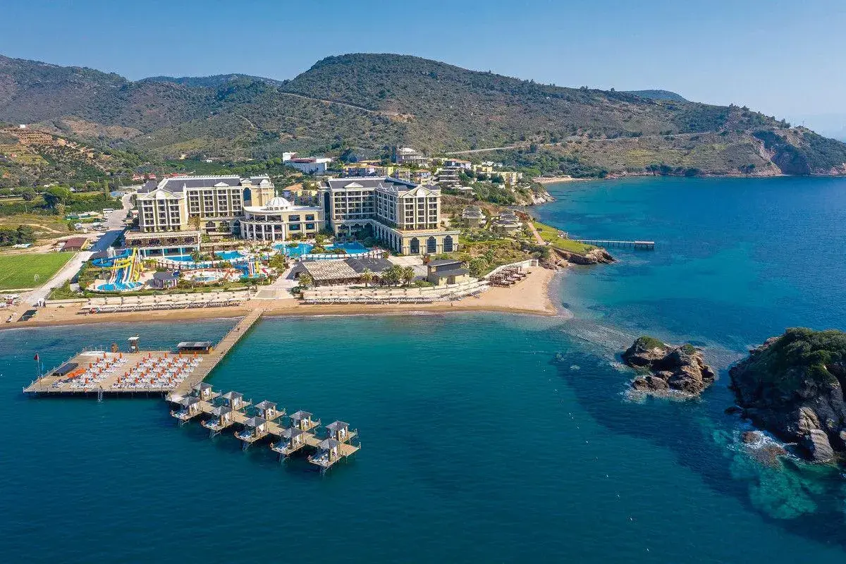 Luftaufnahme des Sune Efes Royal Palace mit Pools, Wasserrutschen und einem Steg mit Liegen am türkisfarbenen Meer.