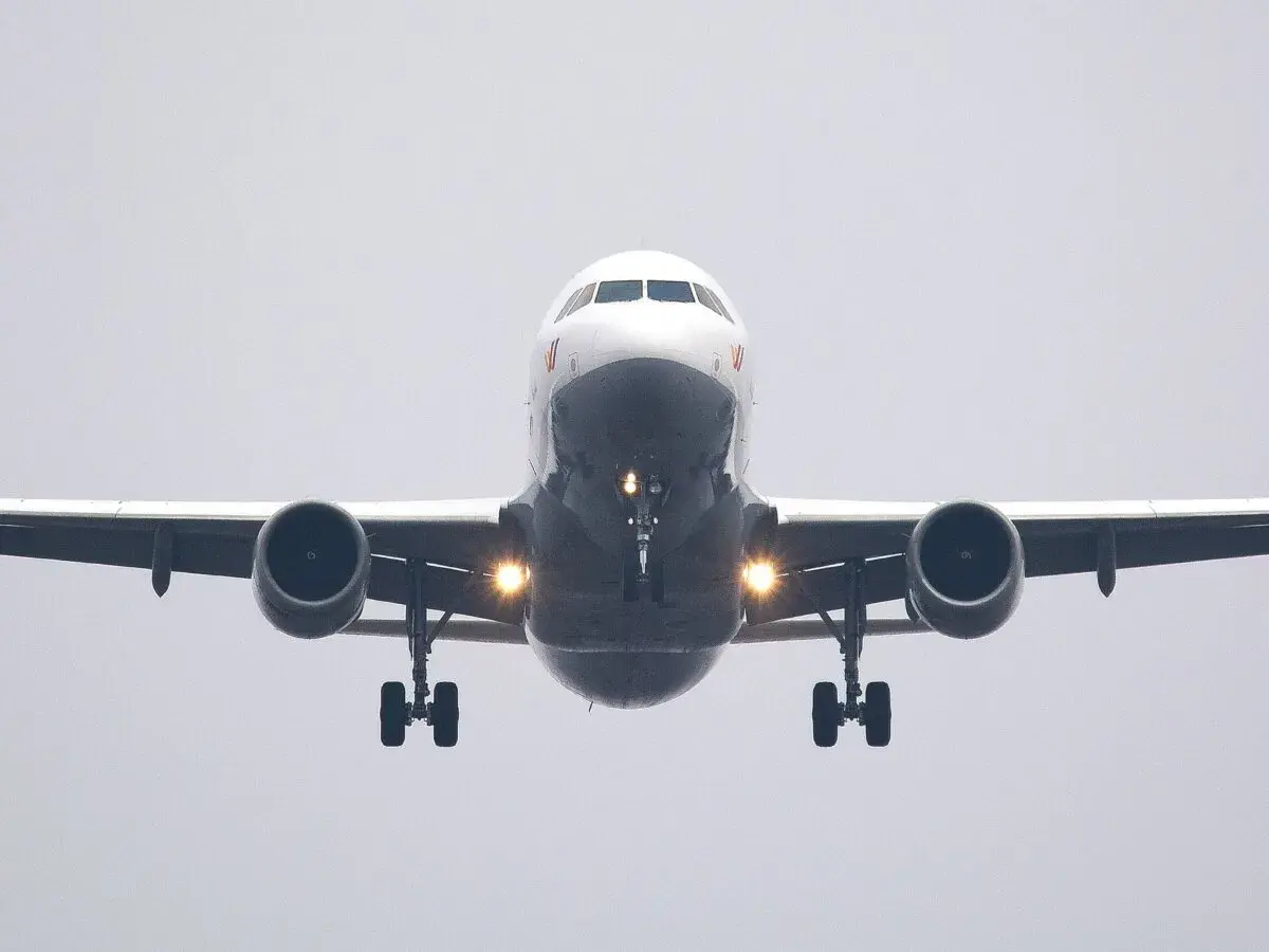 Ein Flugzeug nähert sich mit hoher Geschwindigkeit der Landebahn. Die Lichter am Fahrwerk leuchten hell.