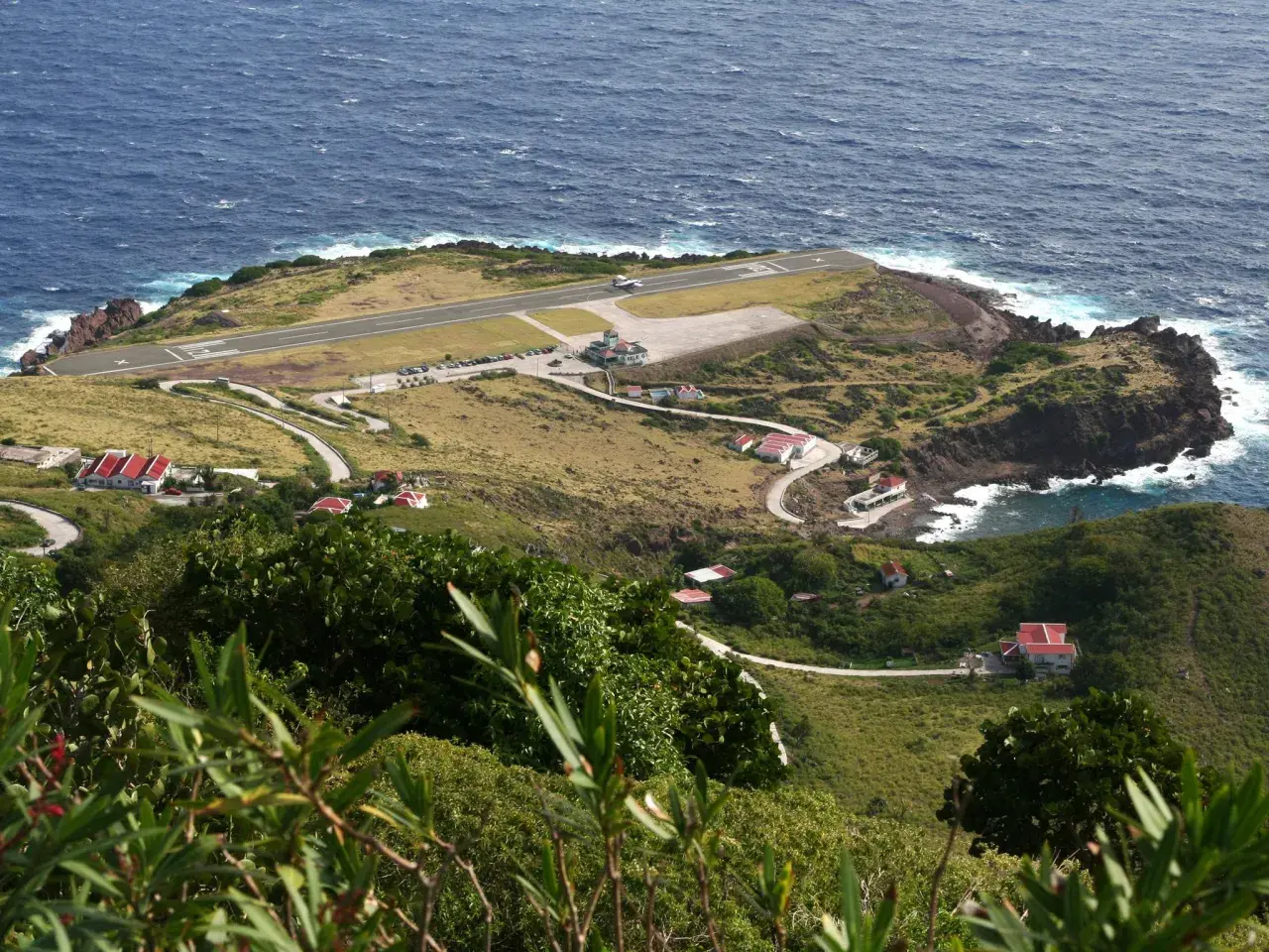 Ein Flugzeug landet auf der Landebahn des kleinsten Flughafens der Welt, umgeben von grünen Hügeln und dem blauen Meer.