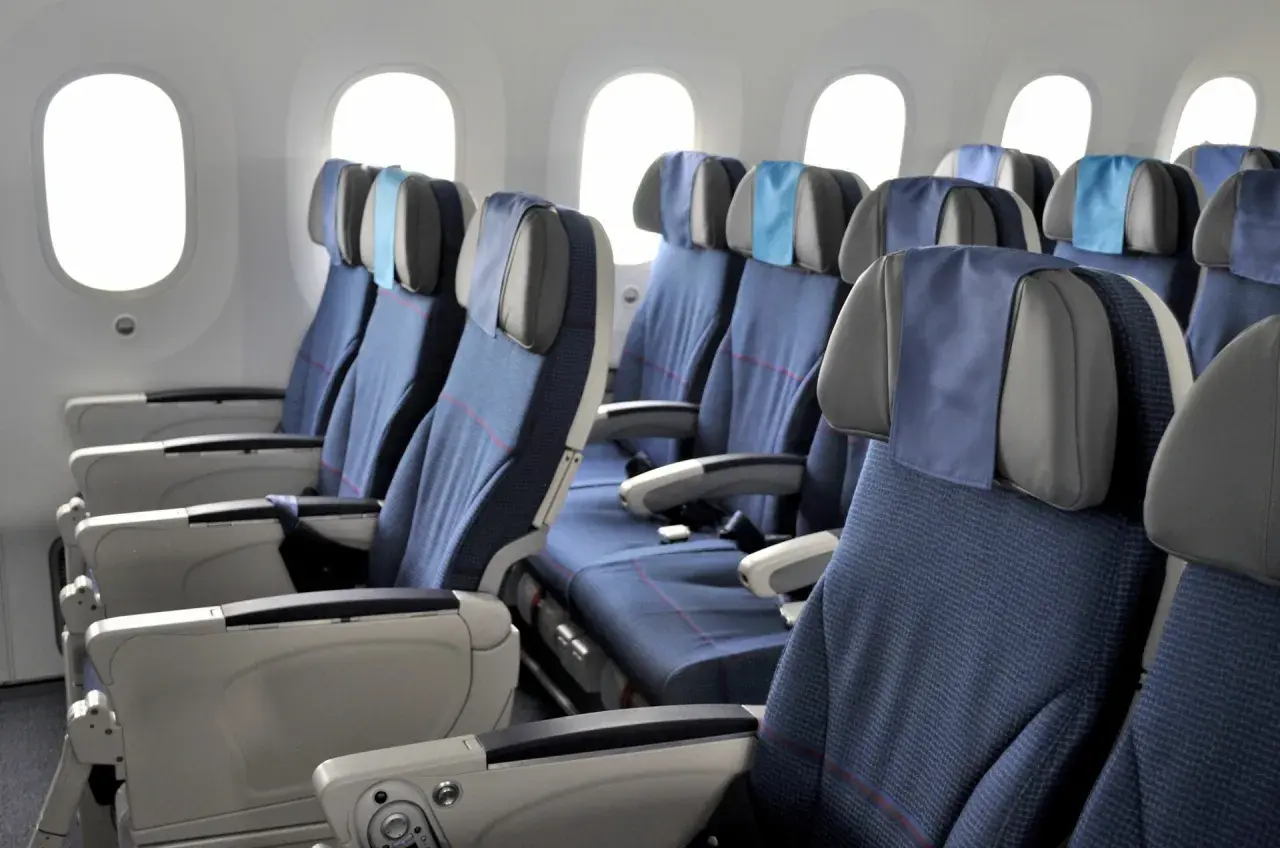 Reihe von blauen Flugzeugsitzen mit Kopfstützen und Armlehnen, daneben Fenster. Ein Fensterplatz im Flugzeug bietet Aussicht.
