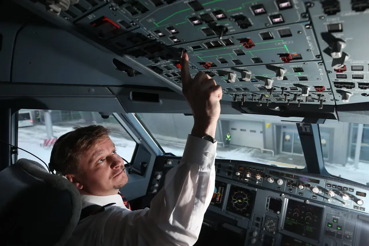 Pilot im Cockpit prüft die Anzeigen. Er bedient einen Schalter, während draußen Schnee liegt.