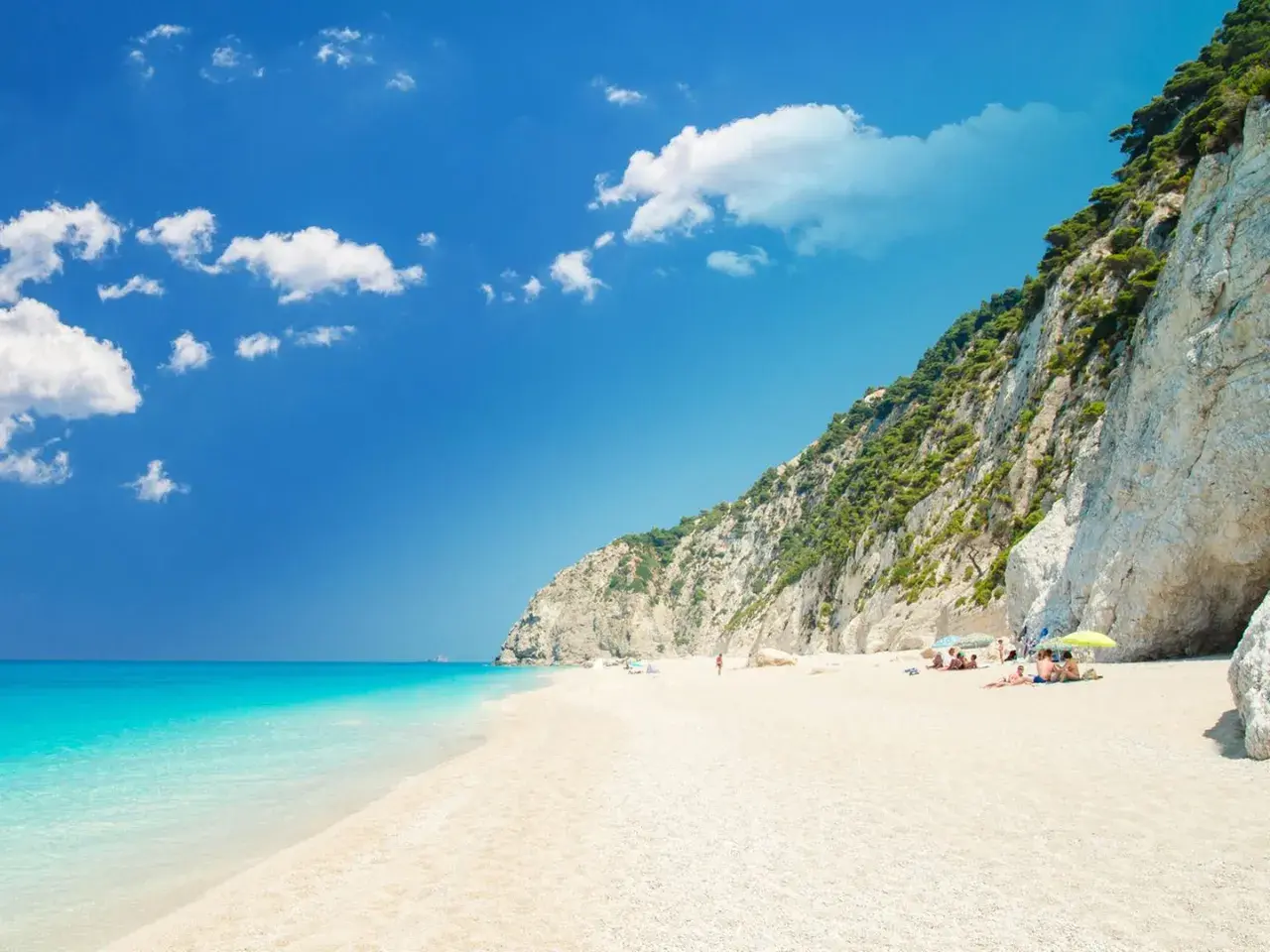 Traumhafter **Griechenland Sandstrand** mit türkisblauem Meer, weißen Klippen und einigen Sonnenanbetern.