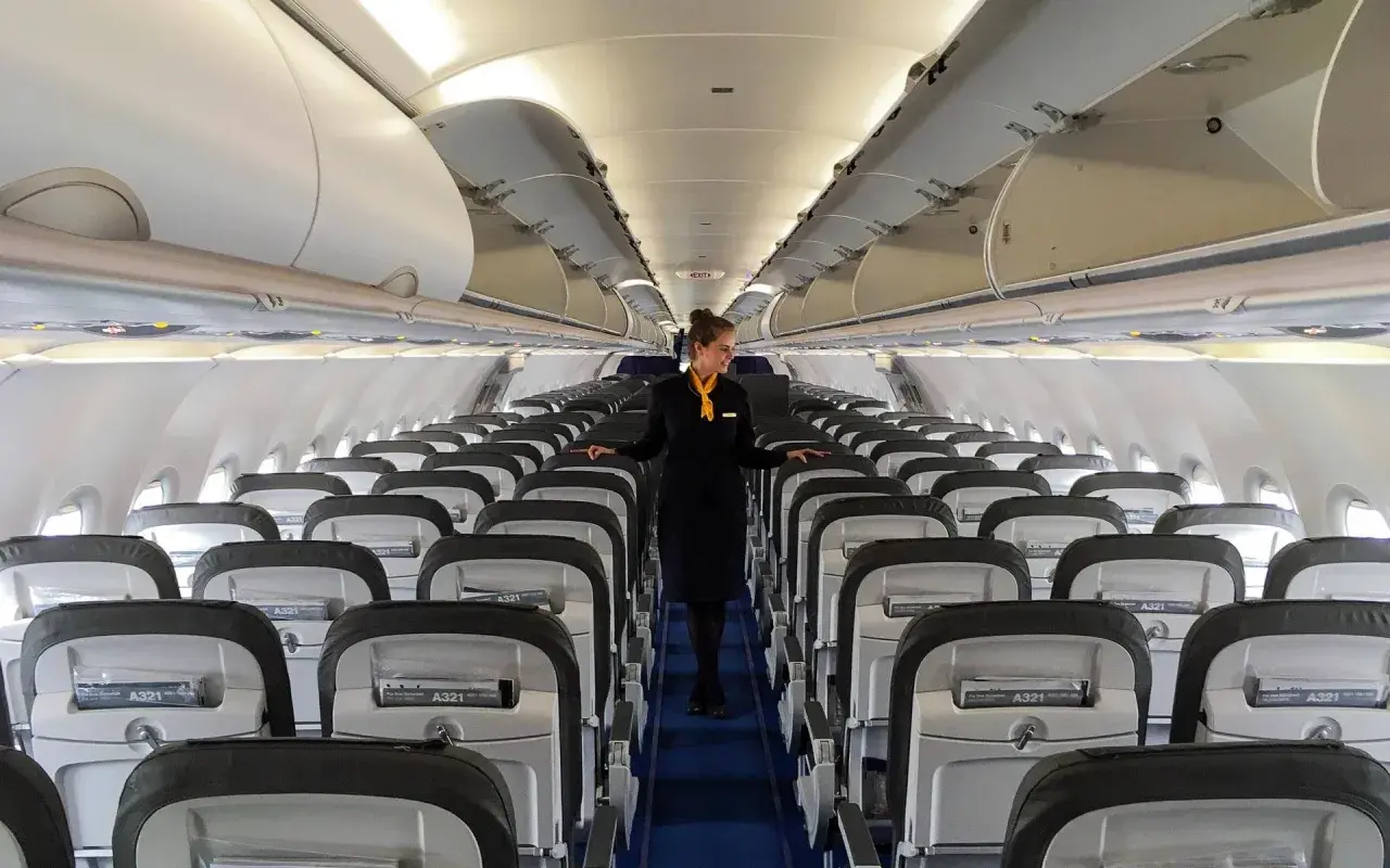 Flugbegleiterin in einem leeren Flugzeug. Die Reihen von Sitzen und die sorgfältige Präsentation lassen die Frage "Ist Lufthansa sicher?" positiv beantworten.