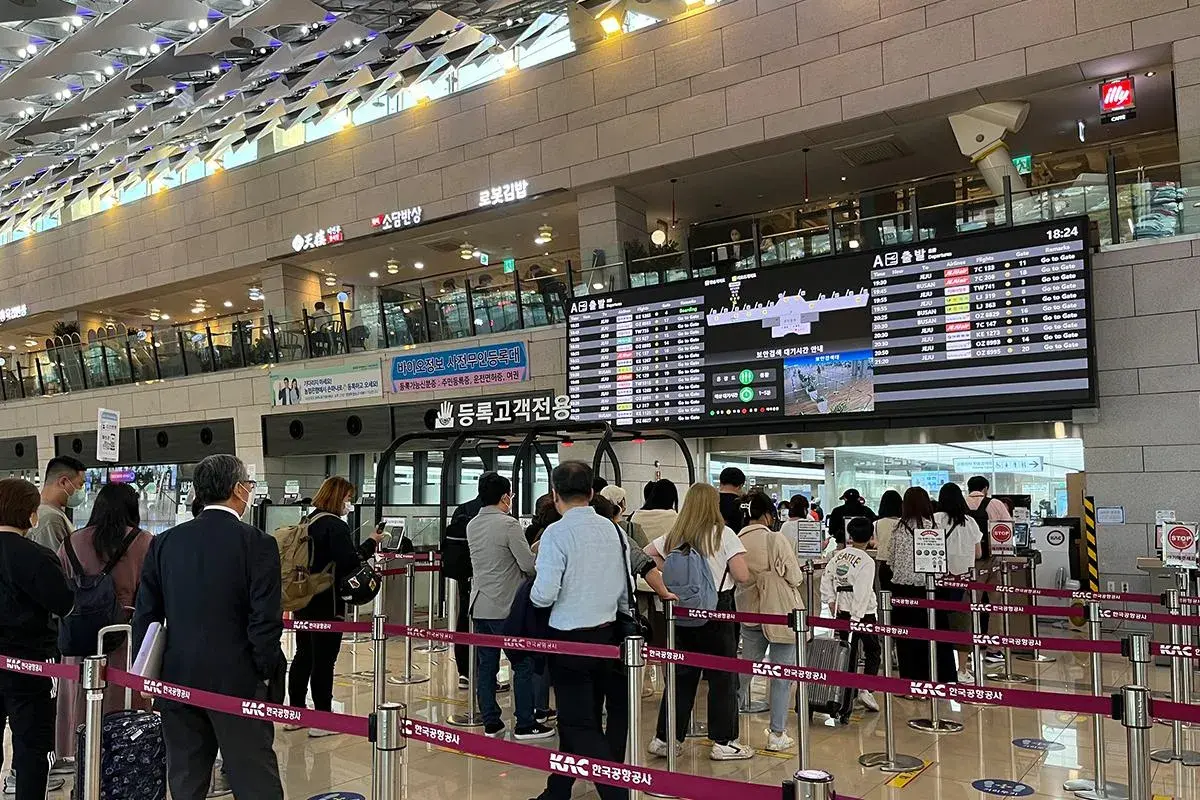 Menschen stehen in einer Schlange am Flughafen Seoul vor einer Anzeigetafel mit Abflugzeiten.