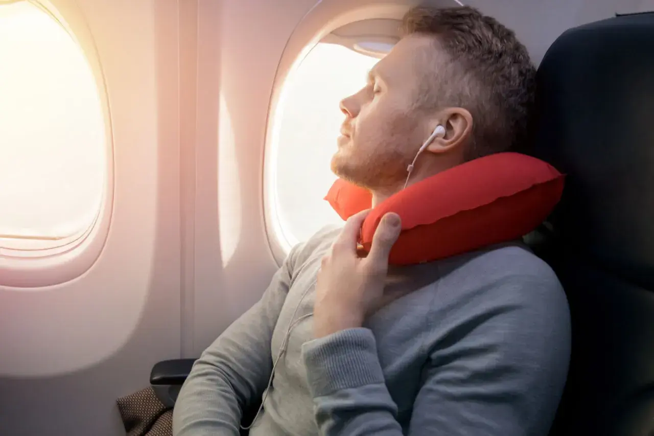 Mann schläft im Flugzeug mit rotem Nackenkissen. Ein Nackenkissen Flugzeug ist sinnvoll für bequemen Schlaf.