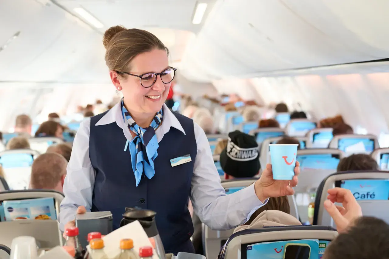 Flugbegleiterin von TUI fly bietet Kaffee an. Ein Lächeln und ein Getränk für die Passagiere.