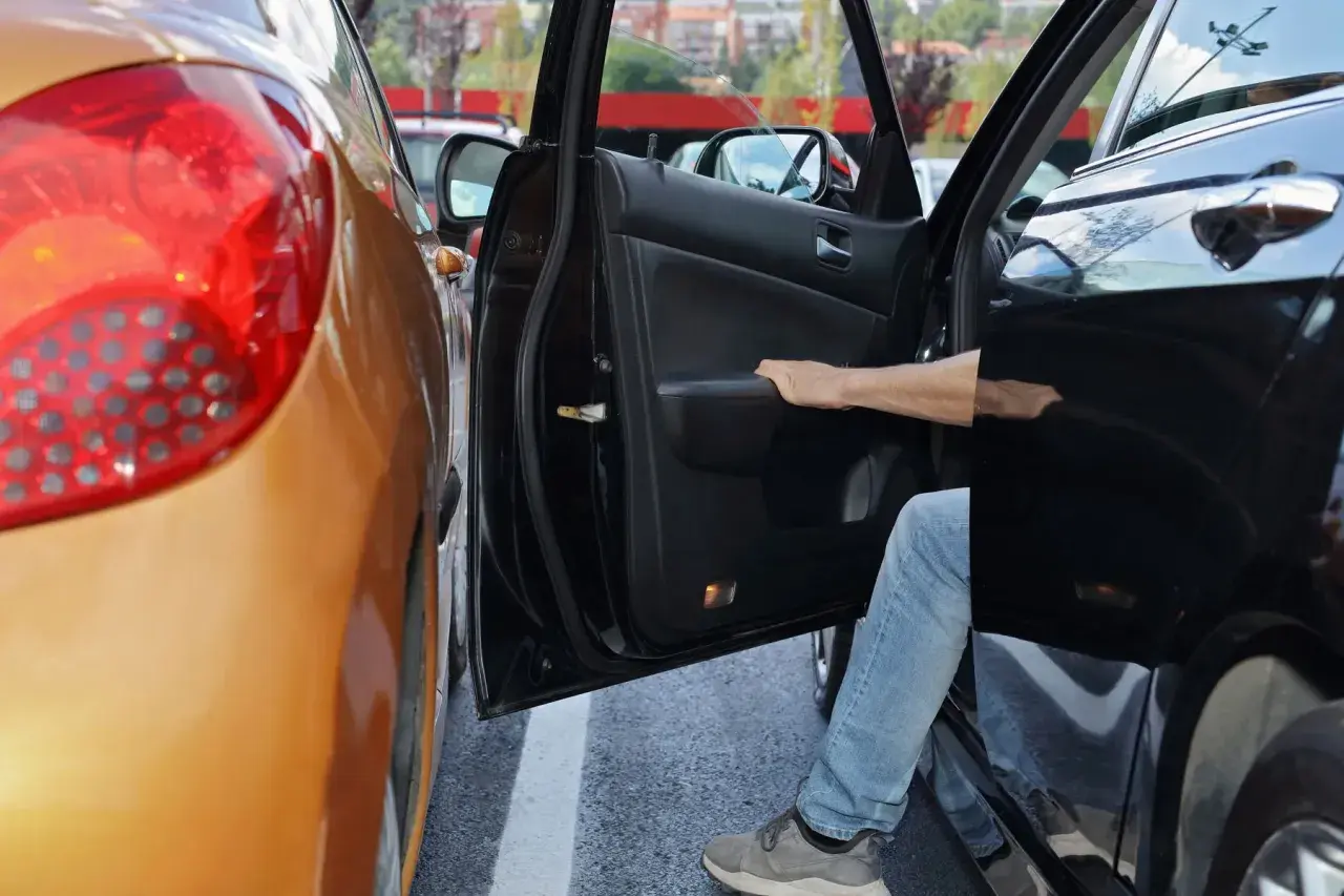 Ein Mann steigt aus seinem Auto, das auf einem Privatparkplatz zu nah an ein anderes Fahrzeug geparkt wurde. Ein kleiner Unfall ist passiert.