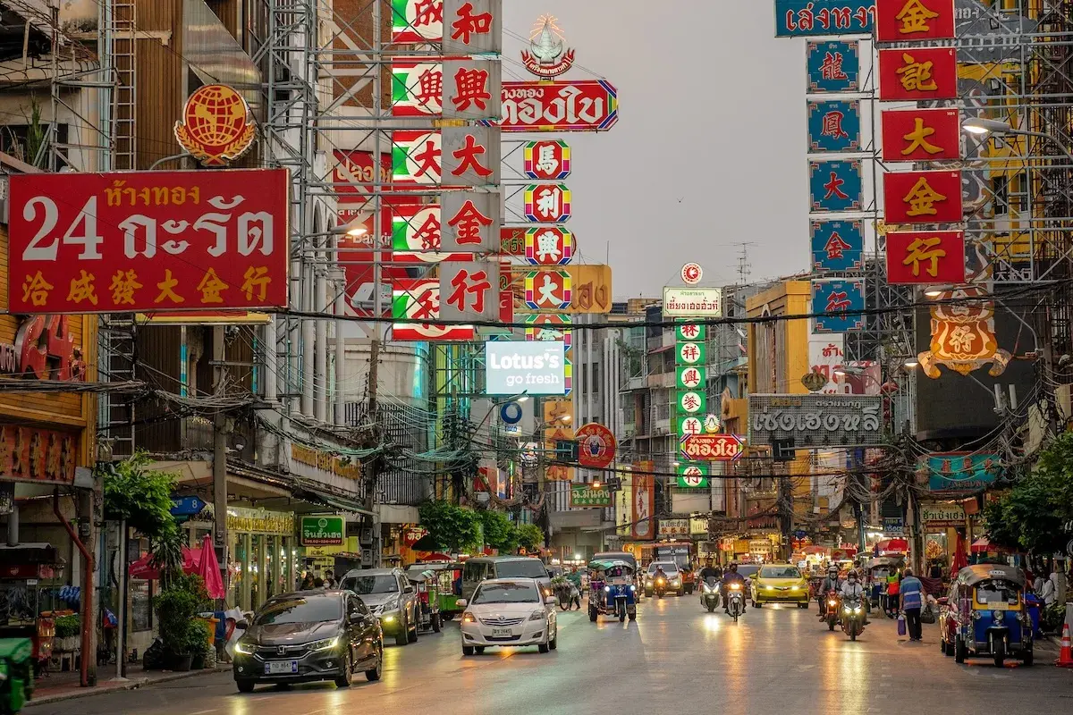 Bunte Neonschilder und Verkehr in Bangkok. Ein lebendiges Bild, das die pulsierende Atmosphäre und die einzigartigen Bangkok Erfahrungen widerspiegelt.