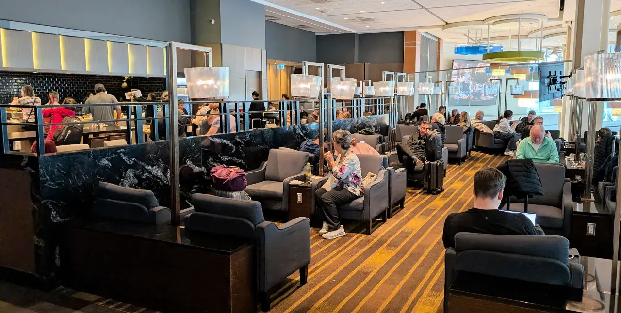 Gemütliche Sitzecken und ein Buffetbereich in einer **priority lounge**. Reisende entspannen sich, arbeiten oder essen.