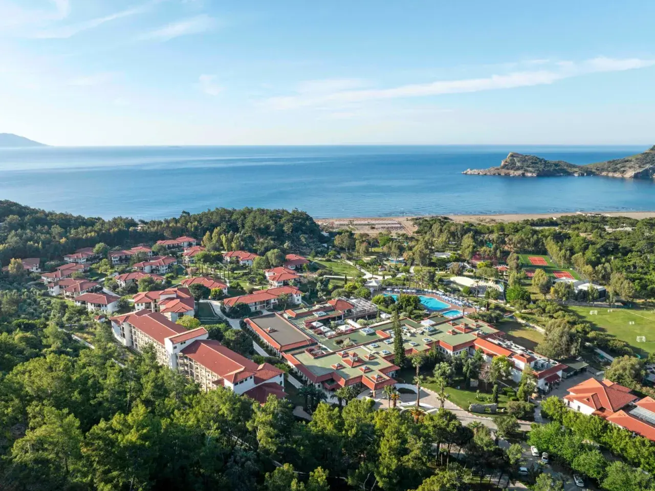 Luftaufnahme des TUI Blue Sarigerme Park mit Blick auf das Meer, Pools und Tennisplätze, eingebettet in üppige grüne Bäume.