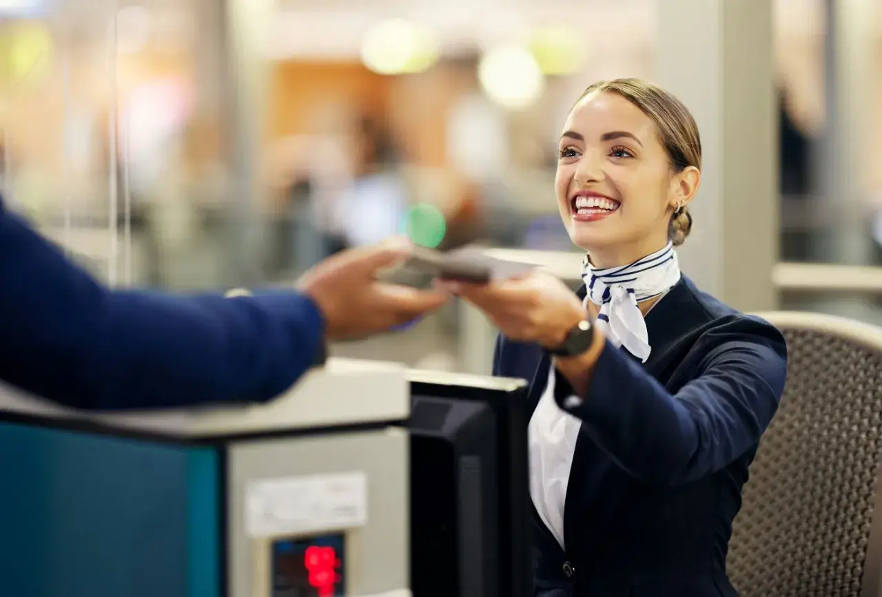 Lächelnde Flugbegleiterin am Schalter reicht einen Pass zurück. Ein Beispiel für Flughafen-Begriffe im Einsatz.