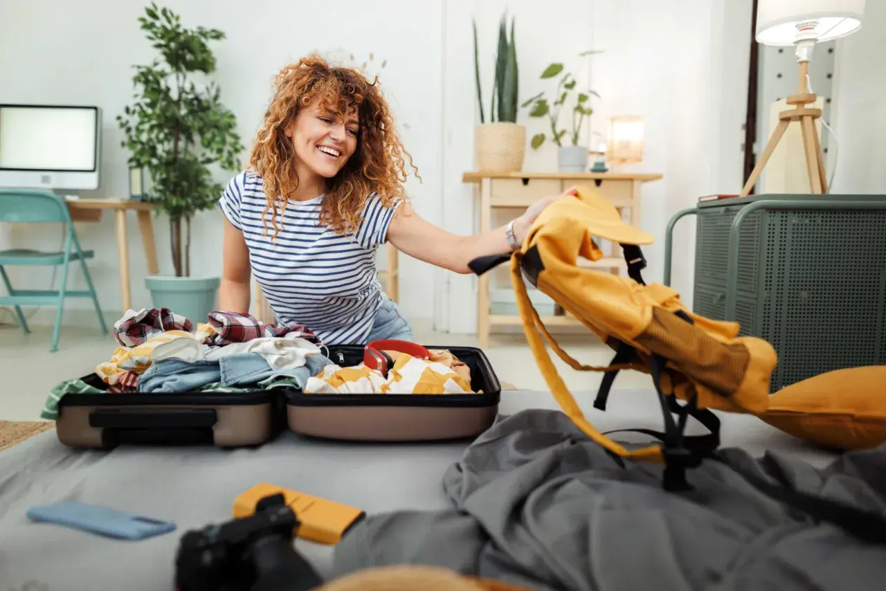 Frau packt Koffer für ihr Auslandssemester. Die Auslandssemester Packliste ist fast komplett, nur noch der gelbe Rucksack fehlt.
