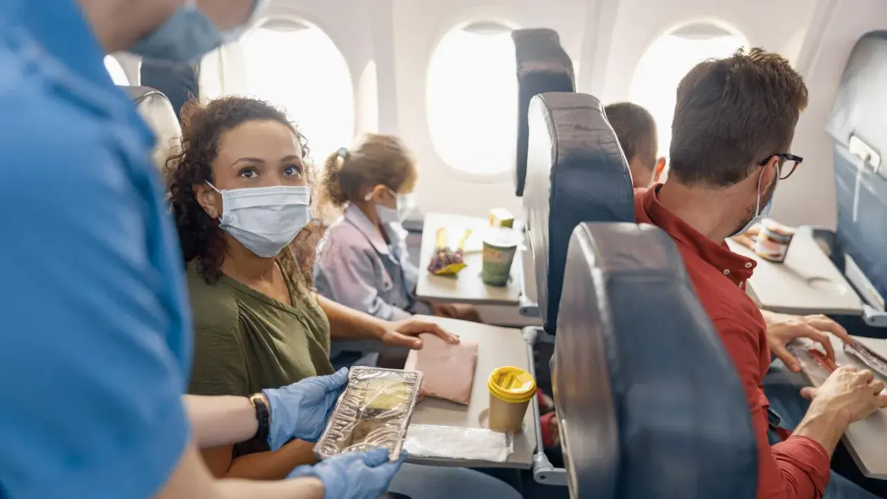 Fliegen mit FFP2-Maske: Eine Frau erhält ihr Essen im Flugzeug. Andere Passagiere tragen ebenfalls Masken.