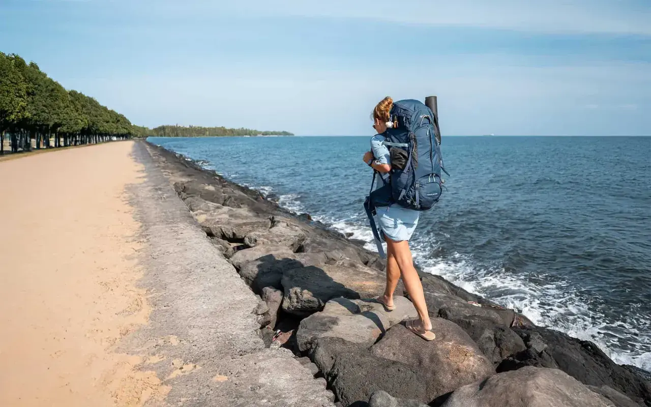 Frau mit großem Rucksack wandert über Felsen am Meer. Perfekte Packliste für Bali!