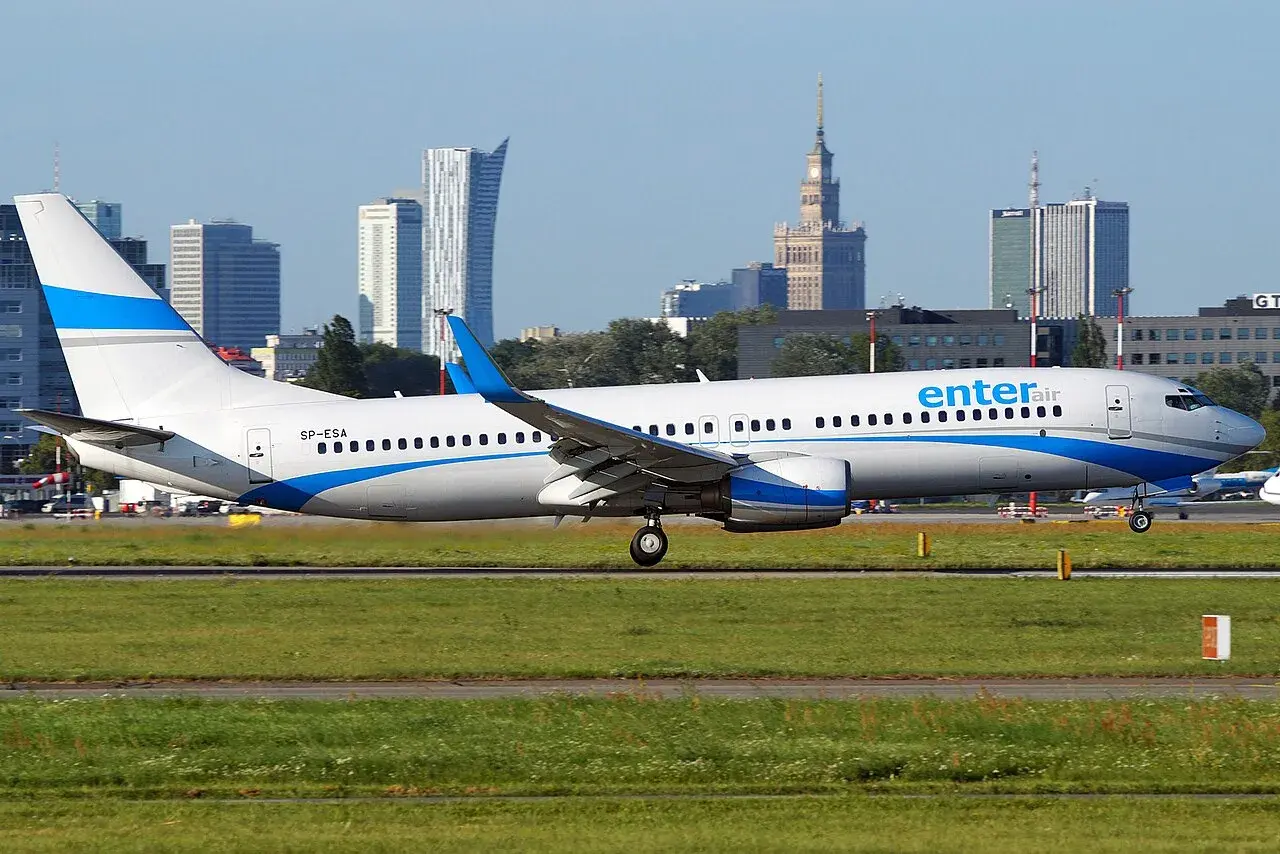 Ein Enter Air Flugzeug rollt auf dem Rollfeld, die Skyline von Warschau im Hintergrund.