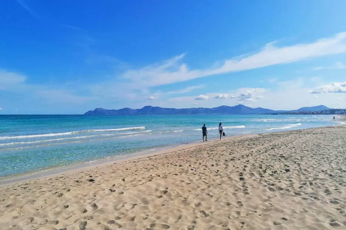 Traumhafter Strand auf Mallorca mit türkisfarbenem Meer und sanften Wellen. Zwei Personen genießen ihren Urlaub.