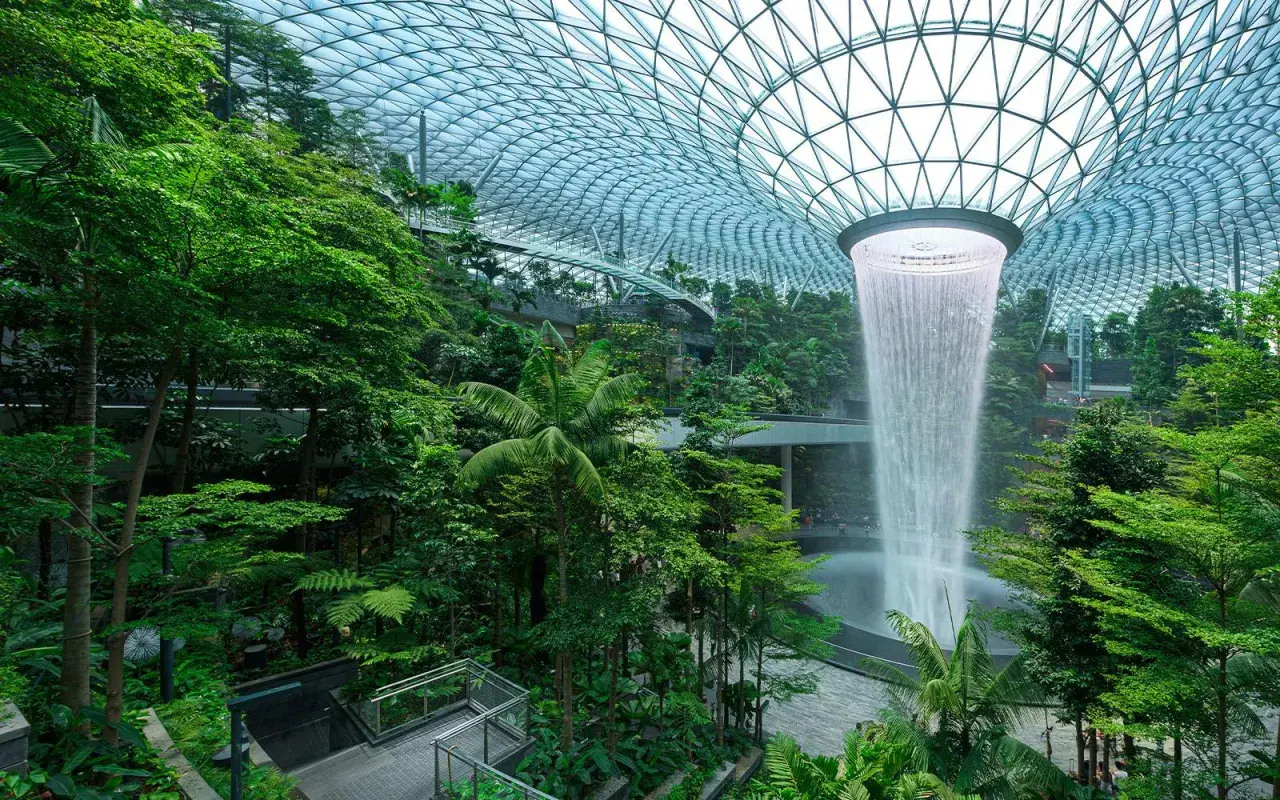 Imposanter Wasserfall im tropischen Garten des Flughafens Singapur. Die beeindruckende Architektur und üppige Vegetation lassen die **Singapur Flughafen Kosten** vergessen.