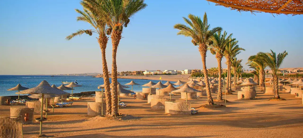 Sonnige Strandkulisse in Hurghada mit Palmen, Sonnenschirmen und Liegen. Perfekt für die Packliste Hurghada!