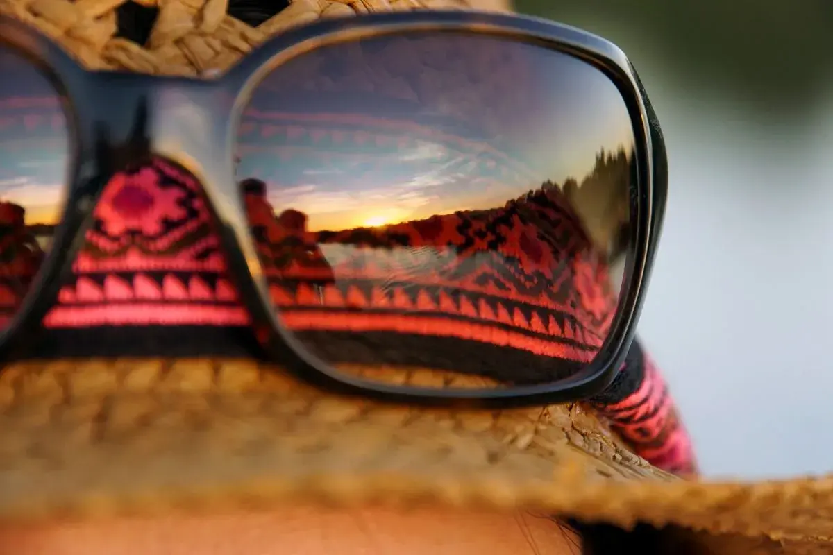 Sonnenuntergangsreflexion in Sonnenbrille auf einem Strohhut. Perfekt für die Packliste Brasilien, mit einem Hauch von Ethno-Muster.