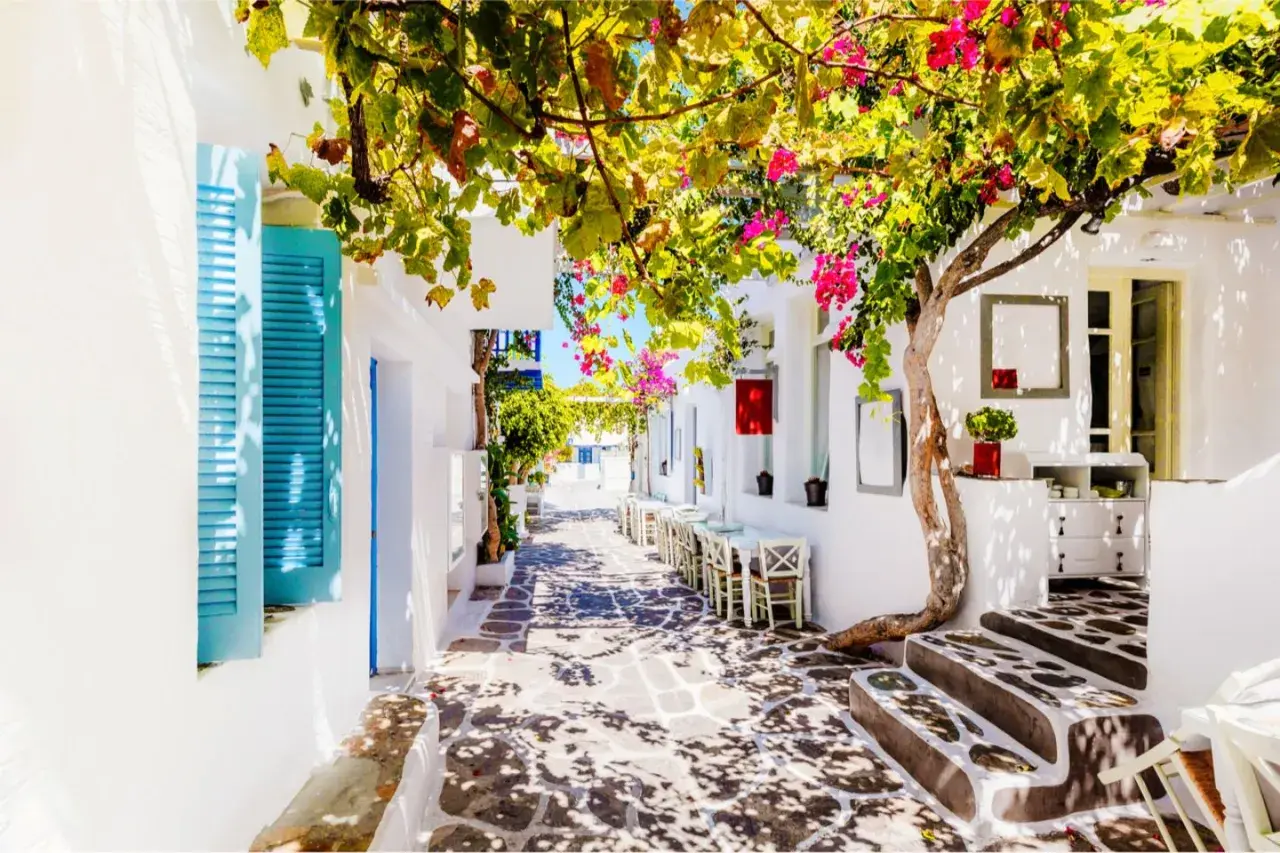 Idyllische Gasse auf Paros, Griechenland, mit blühenden Bougainvillea, weiß getünchten Häusern und Tischen eines Cafés.