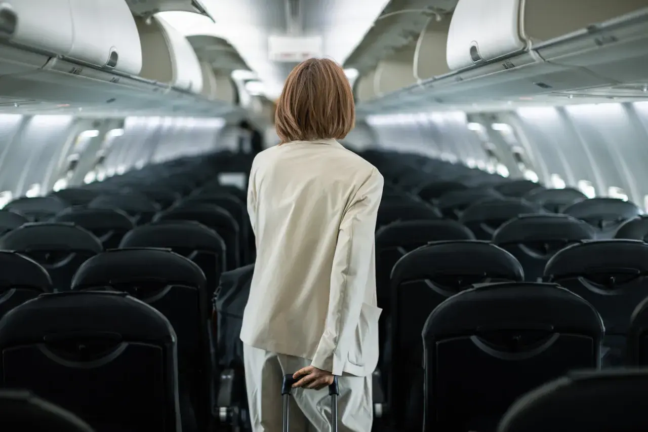 Frau mit Koffer im Gang eines leeren Flugzeugs, bereit für ihren Flug. Sie hat den **priority flughafen** Service gebucht.