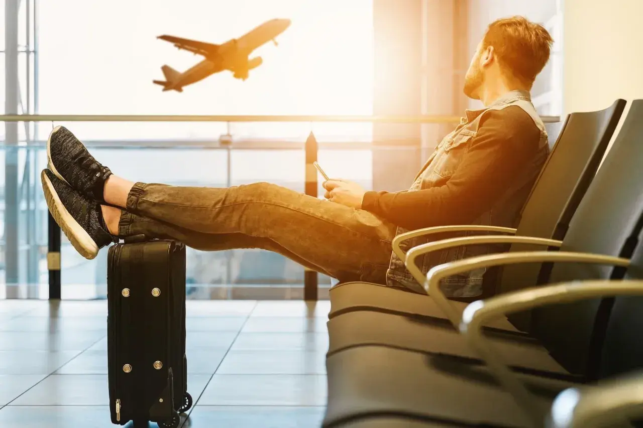Mann mit Füßen auf Koffer wartet im Flughafen auf seinen Langstreckenflug. Ein Flugzeug hebt ab.