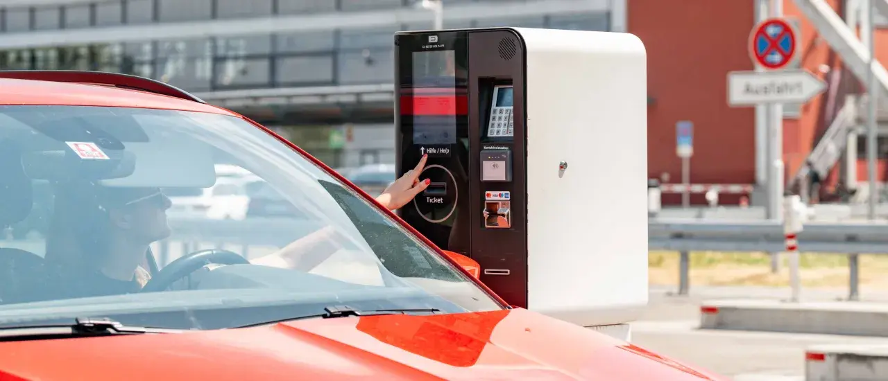 Frau am Parkscheinautomaten am Flughafen Memmingen. Hier kann man kostenlos parken, wenn man den richtigen Tarif wählt.