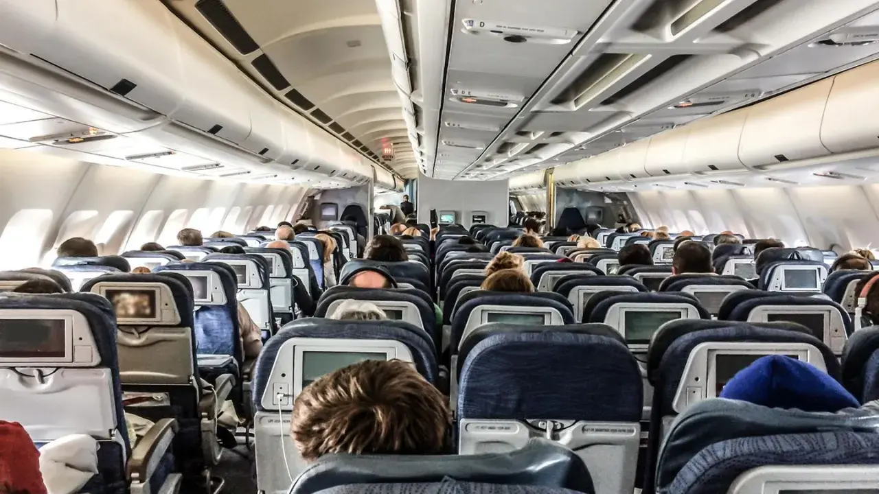 Blick in die Kabine eines Flugzeugs mit vielen Reihen von Langstreckenflug Sitzen, einige mit Bildschirmen.