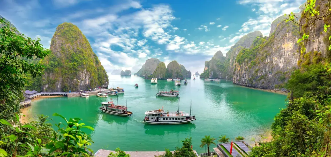 Traumhafte asien reiseziele: Boote gleiten durch smaragdgrünes Wasser, umgeben von steilen, bewachsenen Karstfelsen im Halong-Bucht.