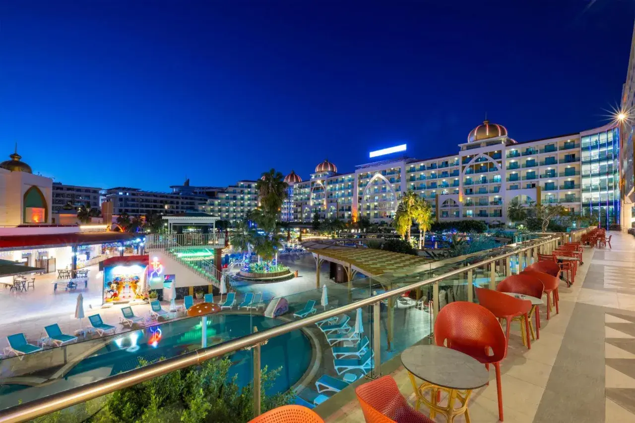 Abendansicht des Alan Xafira Deluxe Resort & Spa mit beleuchteten Pools, Palmen und stilvollen roten Stühlen auf der Terrasse.